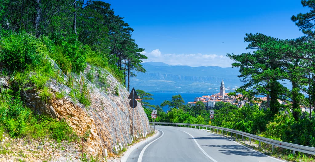 Road leading toward a coastal town on Krk Island surrounded by Mediterranean vegetation